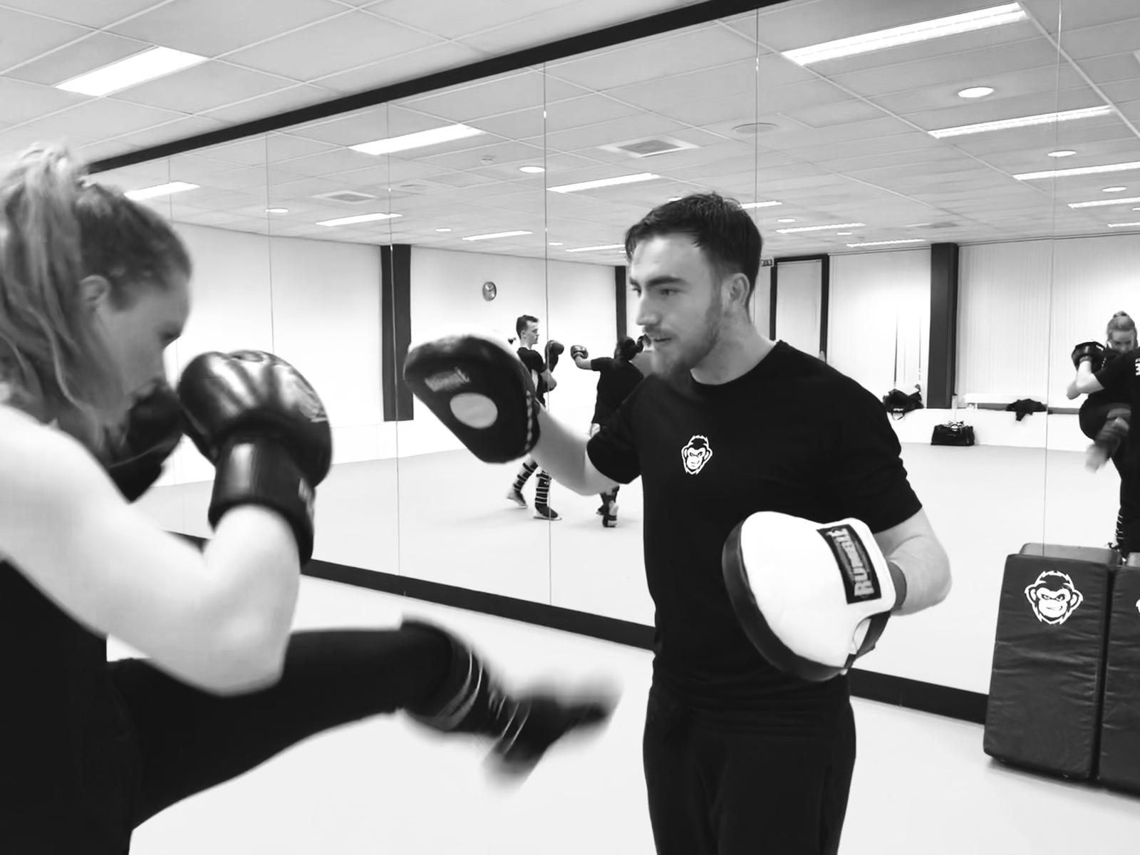 Trainer begeleidt een deelnemer bij het oefenen van een trap tijdens een kickbokstraining in de sportschool